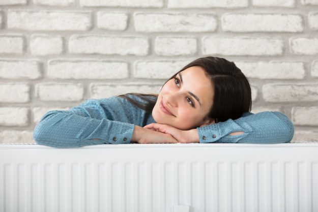 Portrait Of A Smiling Woman Behind The Heating Radiator